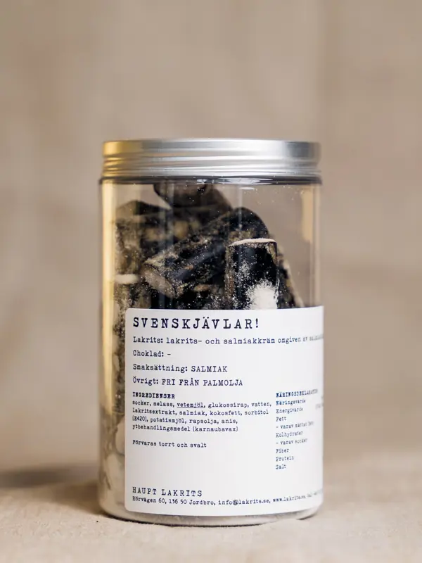 Et glass med 250 gram Svenskjävlar fra Haupt Lakrits – verdens salteste lakris, fylt med salmiakkrem og omgitt av salmiakklakris, presentert i en elegant glasskrukke med hvit etikett.